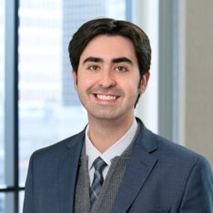 A professional headshot of Lucas Spremulli in front of windows.