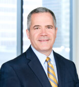 A professional headshot of Robert Brooks in front of windows.