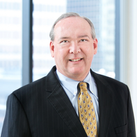 A professional headshot of Mark Denehy in front of windows.