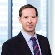 A professional headshot of John Russell in front of windows.